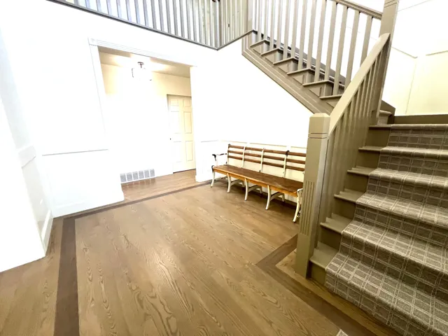 Entryway featuring wood-finish flooring with a dark border inlay, wainscoting details, and a staircase with patterned carpeting and painted wood railings