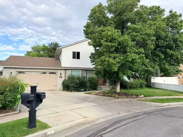 Two-story residence featuring a two-car garage with arched window accents, a pitched shingle roof, and a mature shade tree