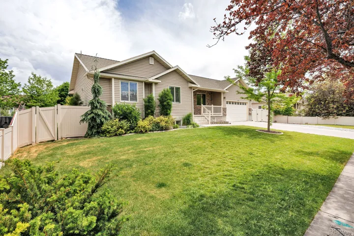 Siding exterior with a two-car garage, manicured lawn, established landscaping, and a privacy fence