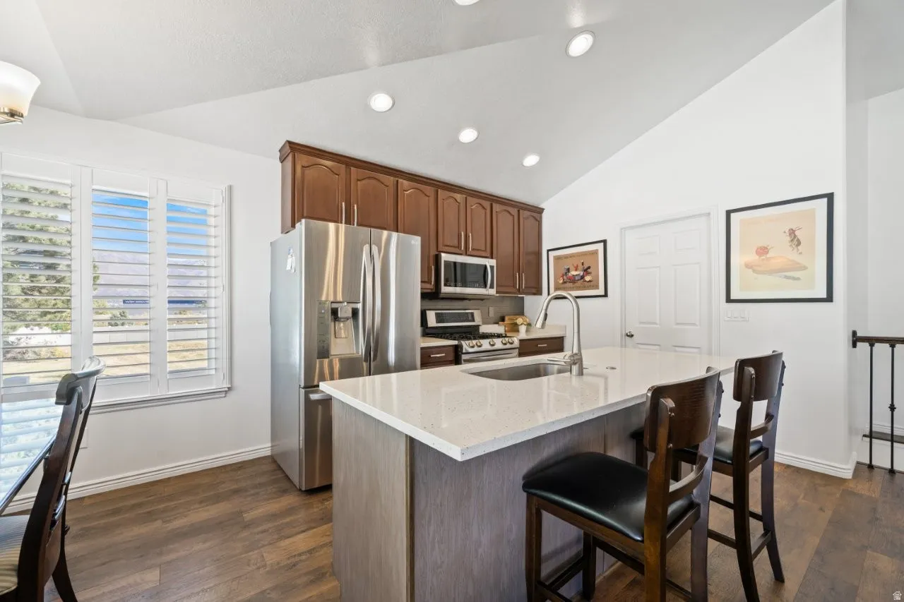 Kitchen featuring stainless steel appliances, light stone counters, a kitchen breakfast bar, a center island with sink, and dark wood-style flooring