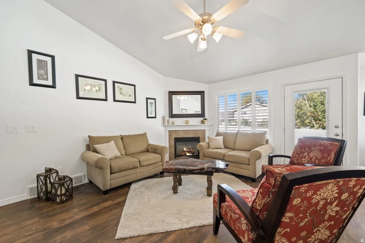 Living room featuring lofted ceiling, dark wood-type flooring, a tile fireplace, and ceiling fan