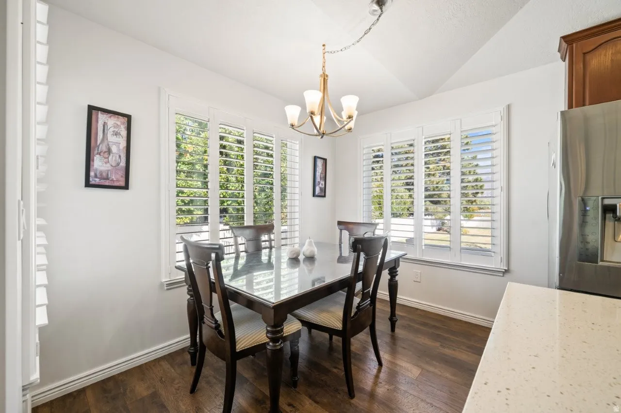 Dining space with dark wood-style floors, vaulted ceiling, and a chandelier