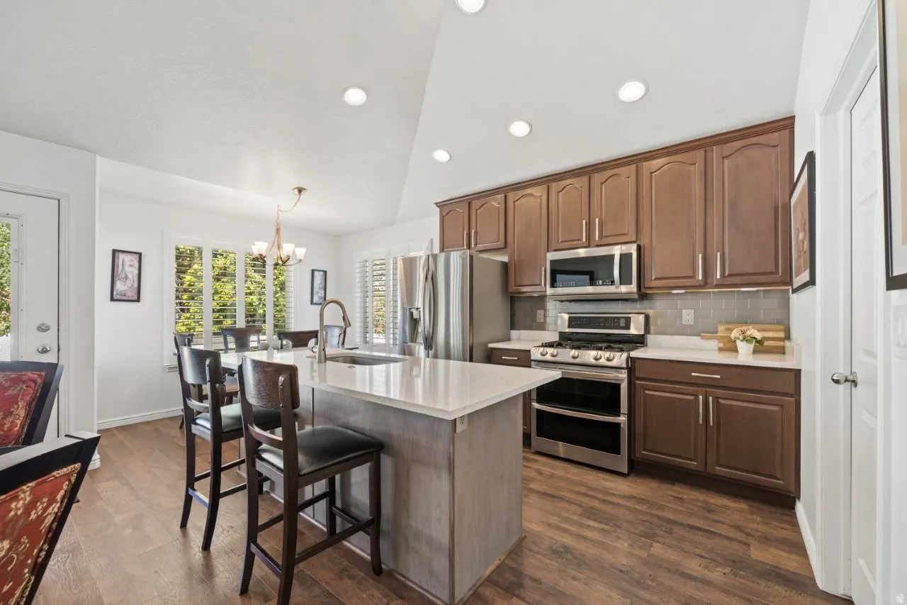 Kitchen with stainless steel appliances, backsplash, lofted ceiling, dark wood-style floors, and a kitchen bar