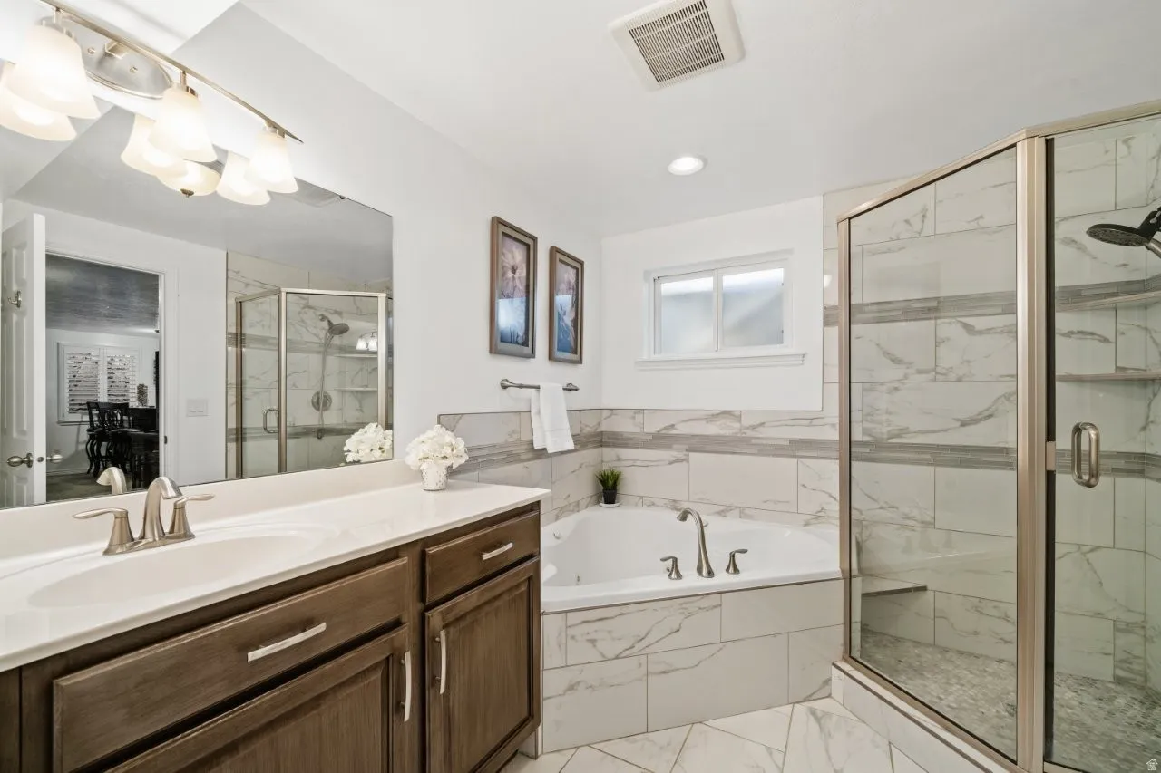 Full bath featuring a bath, a marble finish shower, vanity, light marble finish floors, and recessed lighting