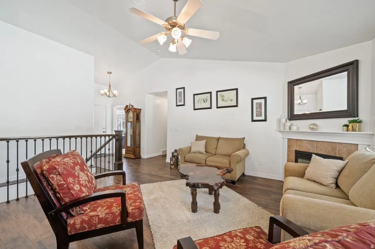 Living room with dark wood-style floors, a chandelier, a fireplace, ceiling fan, and high vaulted ceiling