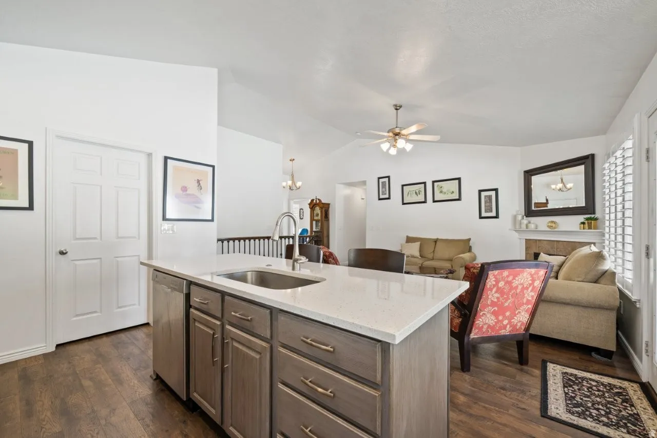 Kitchen featuring vaulted ceiling, dark wood-style floors, light stone countertops, open floor plan, and ceiling fan