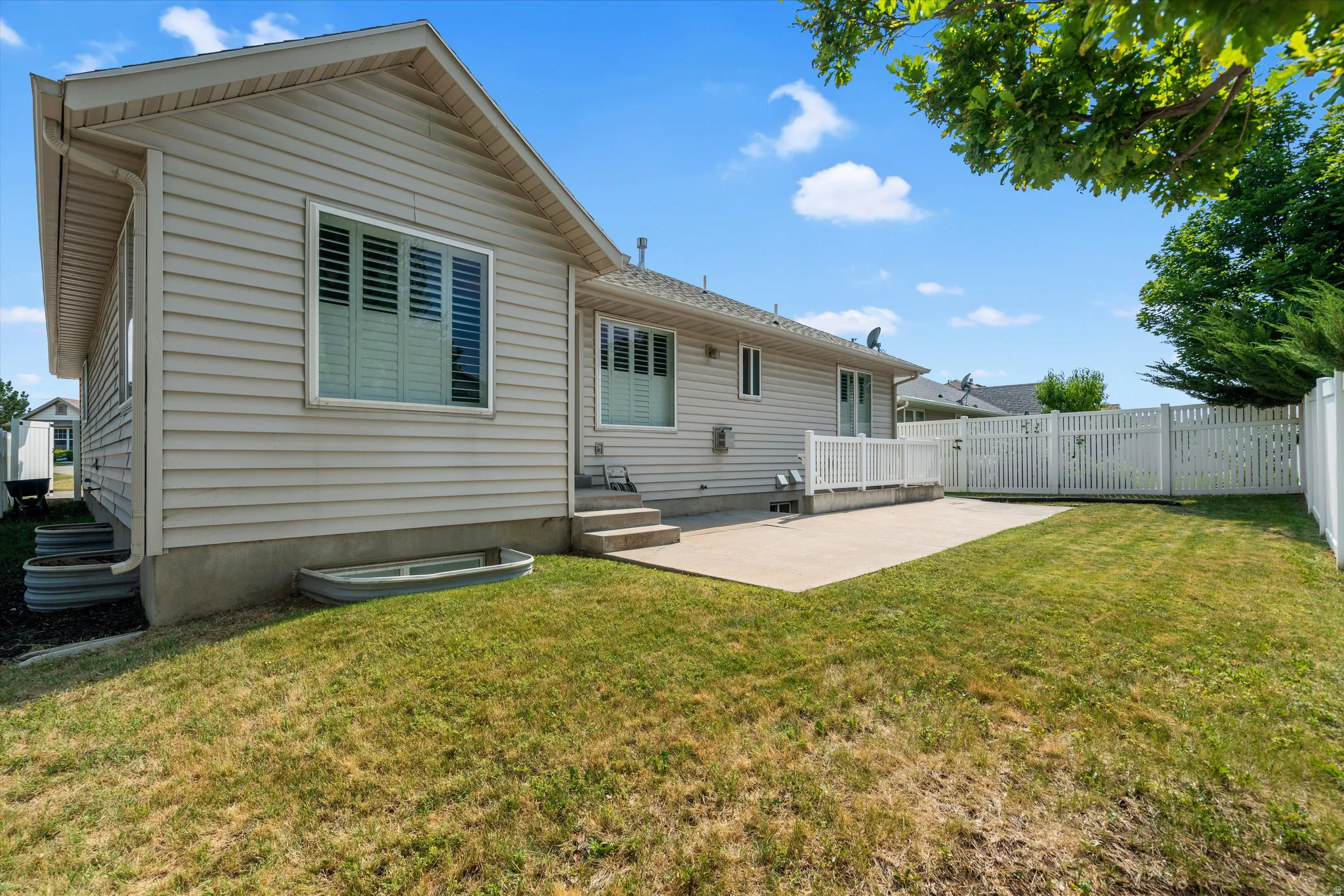 Expansive backyard featuring a concrete patio, a full white picket fence, and mature perimeter trees