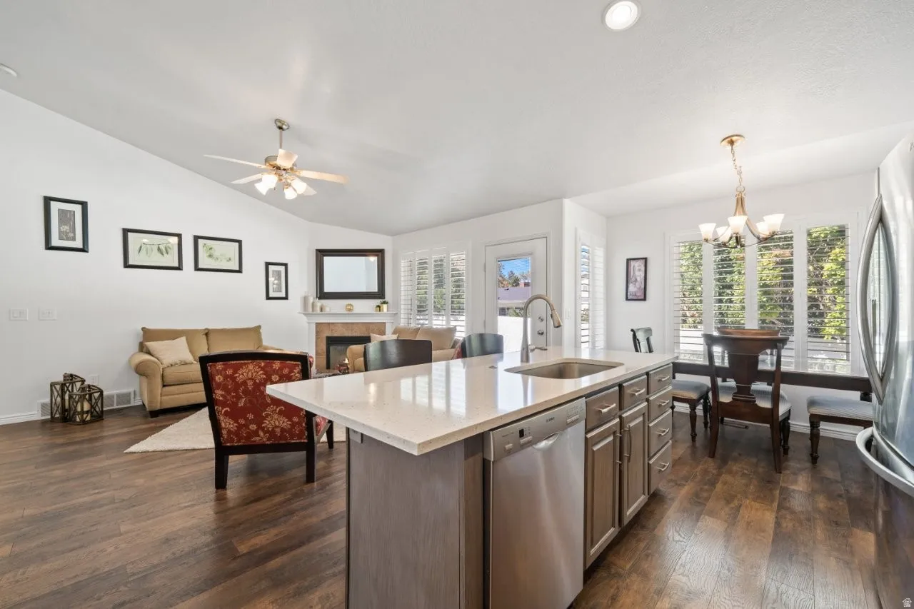 Kitchen with light stone counters, lofted ceiling, appliances with stainless steel finishes, an island with sink, and decorative light fixtures