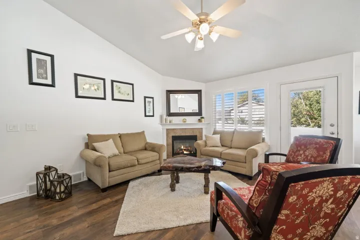 Living room featuring lofted ceiling, dark wood-type flooring, a tile fireplace, and ceiling fan