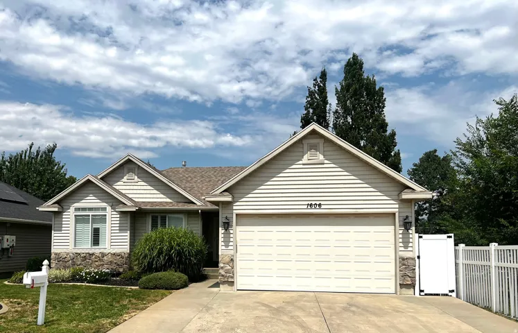 Siding exterior with stone accents, attached two-car garage, and a white picket fence