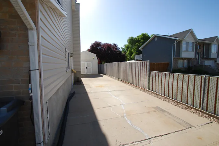 Concrete driveway with a vinyl-sided shed, chain link fencing, and an exterior side entrance