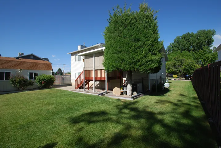 Expansive backyard featuring a manicured lawn, a two-story home with white siding, and a wooden deck with red-stained stairs