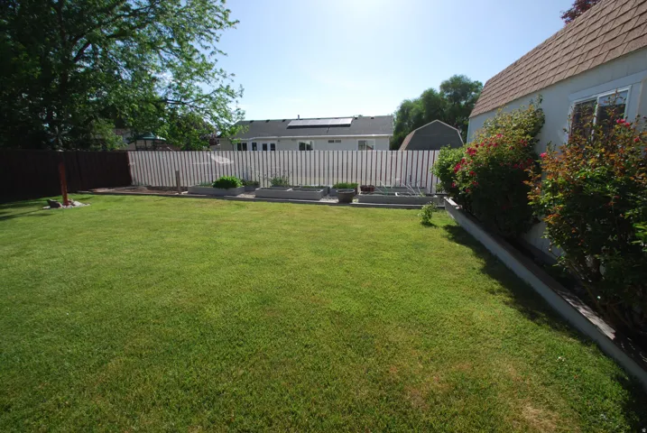 Spacious rear yard featuring an expansive lawn, white privacy fencing, and mature perimeter landscaping