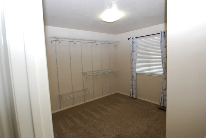 Room featuring neutral-toned carpet, a window with horizontal blinds, and a built-in wire shelving system for storage