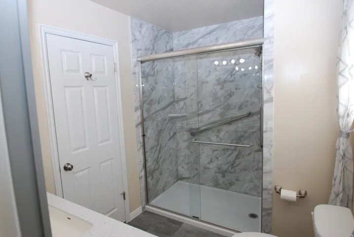 Shower enclosure with sliding glass door and marble-patterned wall panels