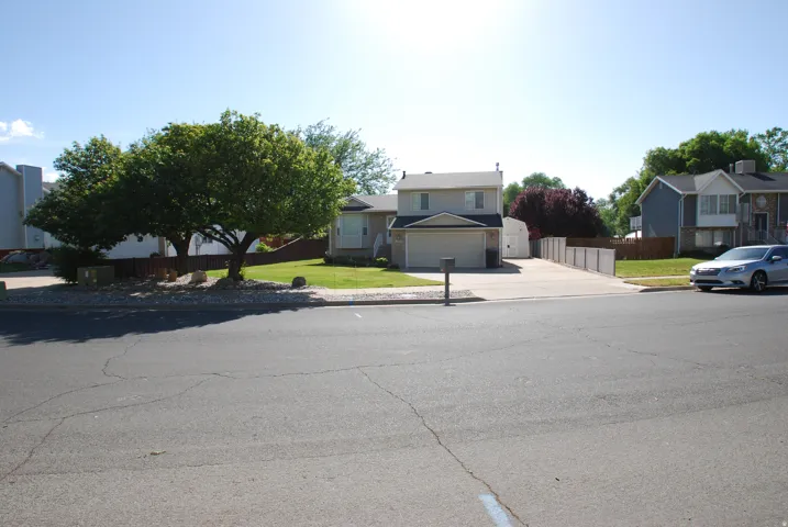 Two-story residence with an attached garage, featuring a long driveway, a white storage shed, and a fenced side yard