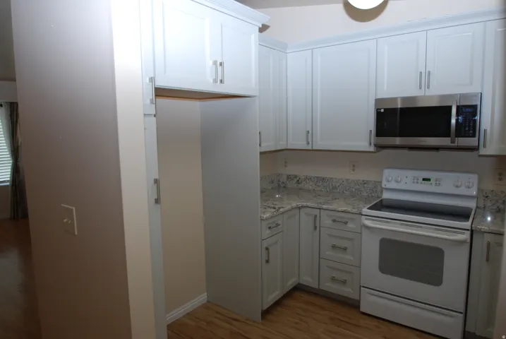 Kitchen featuring light-toned cabinetry with brushed nickel hardware, granite-style countertops, wood-finish flooring, a stainless steel over-the-range microwave, and a white electric range