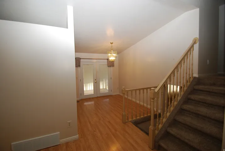 Open-concept interior featuring wood-finish flooring, a chandelier light fixture, and a carpeted staircase with a wood banister