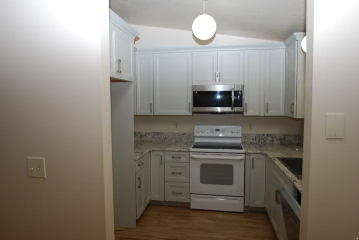 U-shaped kitchen featuring wood-finish flooring, light gray cabinetry with brushed nickel hardware, speckled countertops, and a full suite of appliances including a stainless steel microwave and white range