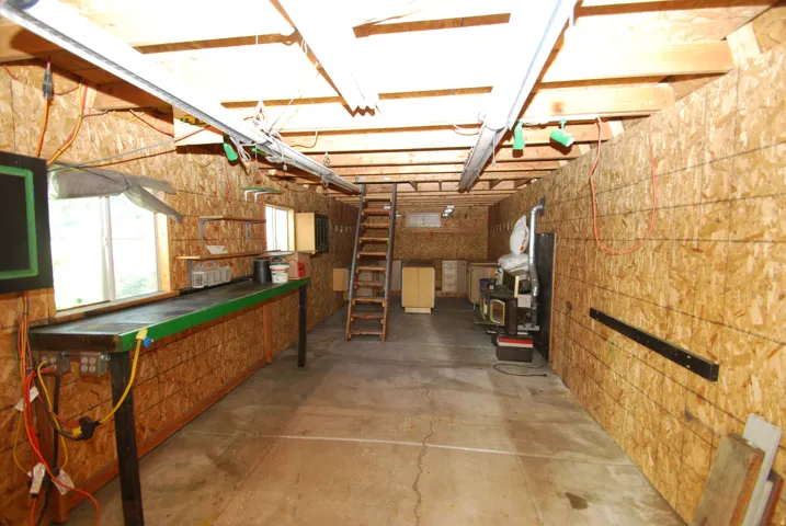 Expansive utility space featuring exposed wood beam ceilings, concrete flooring, dual windows, and built-in shelving