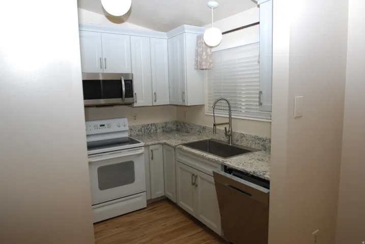 Kitchen featuring white cabinetry, light-toned countertops, wood-finish flooring, stainless steel microwave, and stainless steel dishwasher