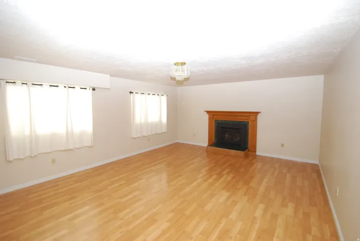 Spacious room featuring wood-finish flooring, a fireplace with a wood mantle and dark stone hearth, and multiple windows