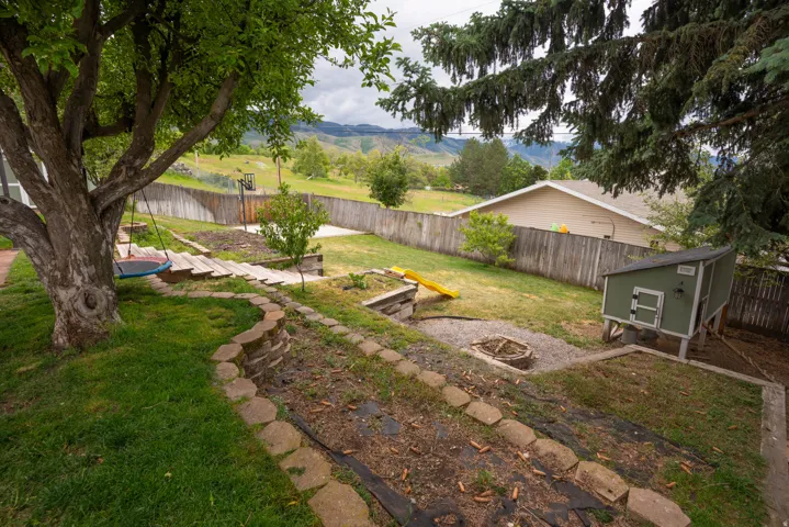 Tiered backyard featuring a large mature tree, a privacy fence, and a gravel fire pit area