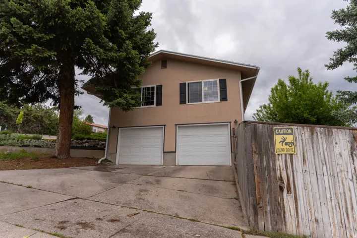 Stucco exterior featuring two garage bays upper-level windows, and mature trees