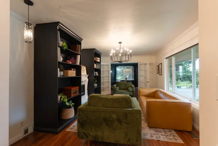 Living area featuring wood-finish flooring, a contemporary chandelier, built-in shelving, crown molding, and large windows  You'll love this updated living room !