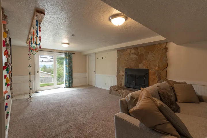 Expansive carpeted room featuring a stone-clad fireplace with a hearth, white wainscoting, and a sliding glass door for exterior access