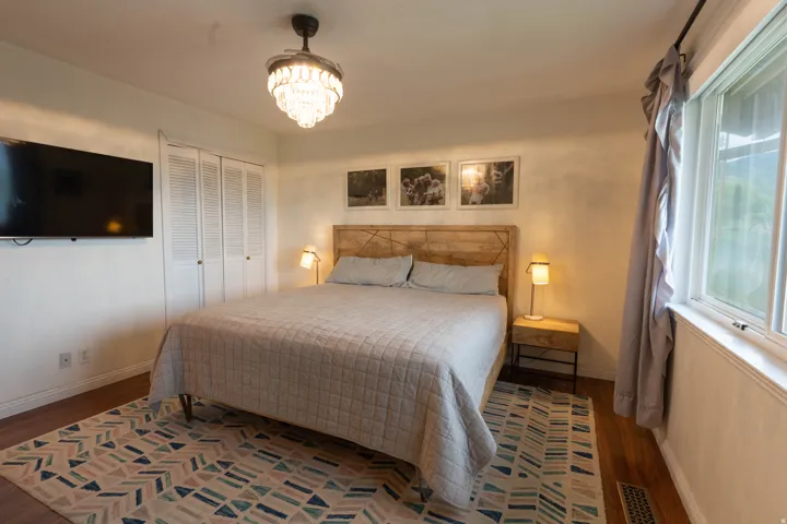 Bedroom featuring wood-finish flooring, a crystal chandelier, and a large window with white trim, double closets too!