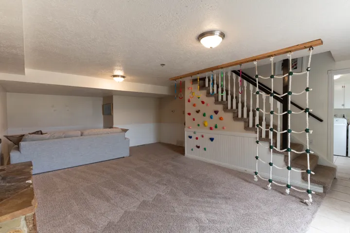 Spacious lower-level area featuring neutral carpet, a decorative staircase with a climbing net, and wainscoting