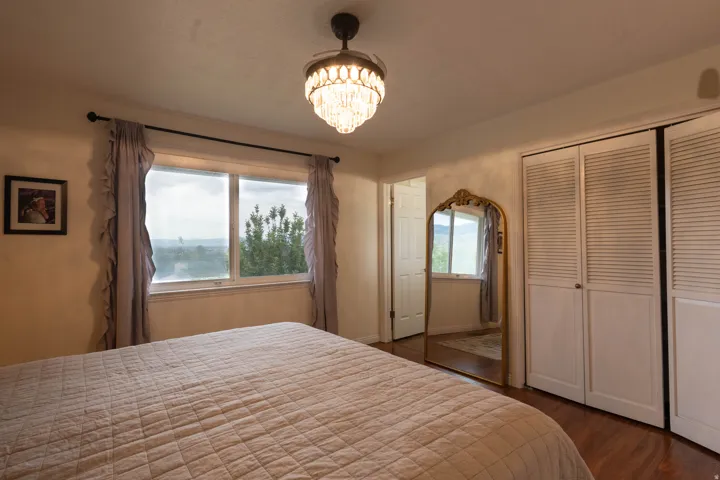 Bedroom featuring a large double window, wood-finish flooring, a decorative chandelier, and louvered bifold closet doors