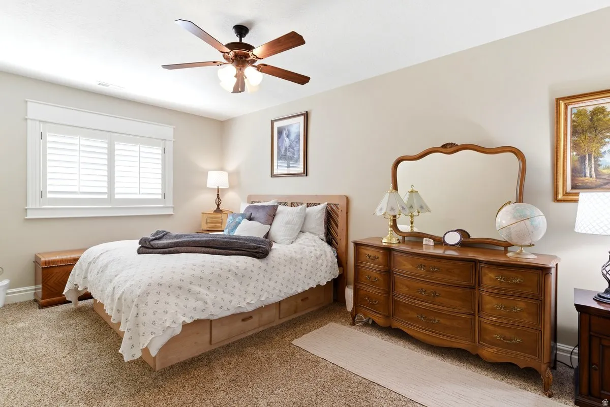 Carpeted room featuring a ceiling fan with light fixture, window with white plantation shutters and trim, and neutral wall paint