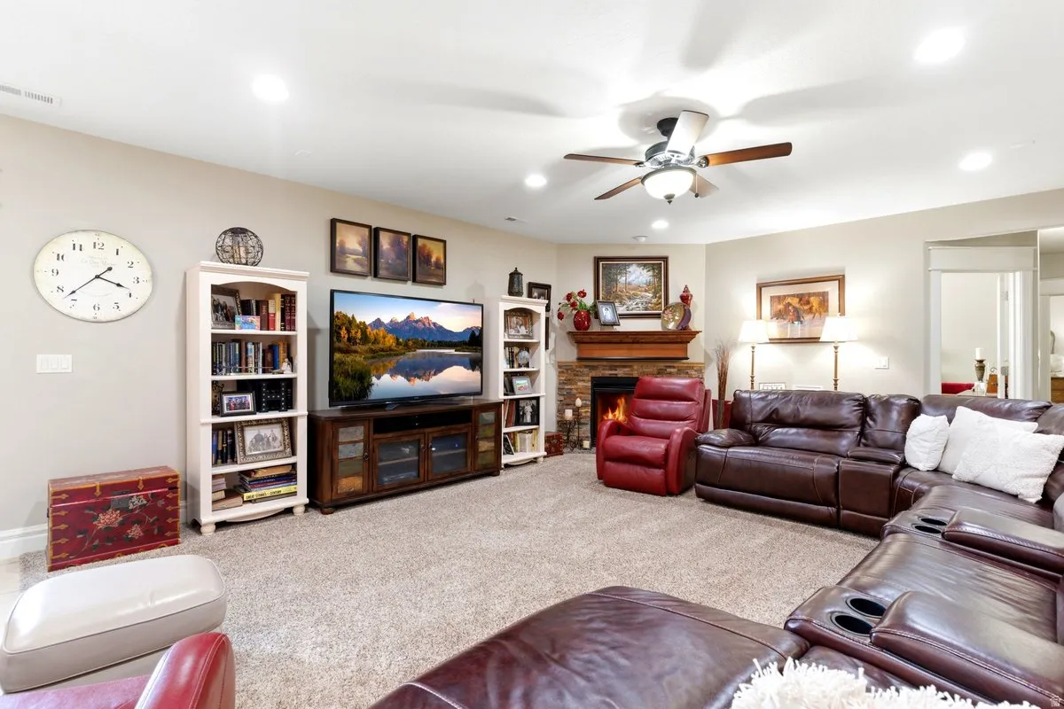 Carpeted living area featuring a stone-faced fireplace with a wood mantel, recessed lighting, and a ceiling fan with light fixture