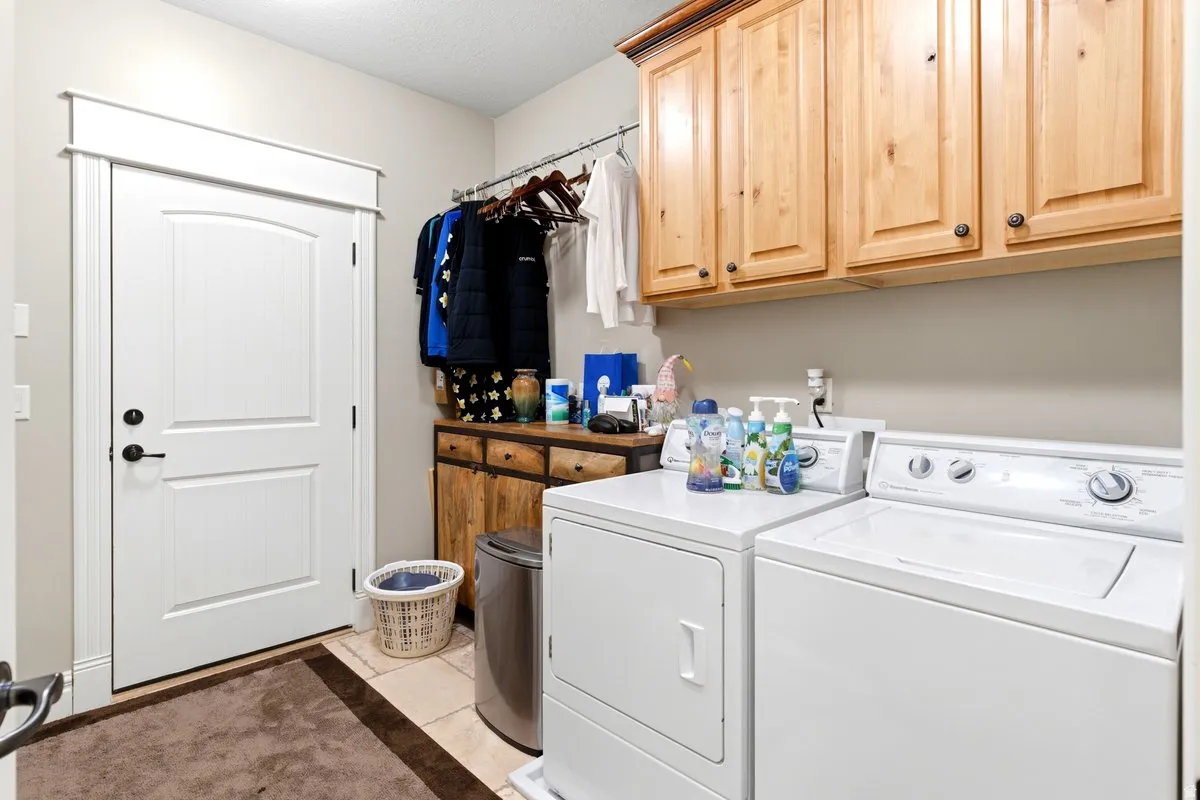 Laundry area featuring upper wood cabinetry, a utility sink, a hanging rod, and light-toned tile flooring