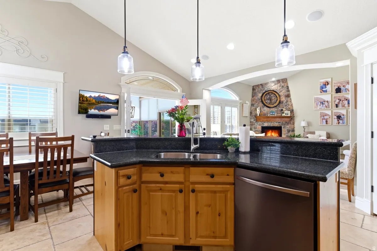Kitchen island featuring a stainless steel sink, dark stone countertop, light wood cabinetry, and a black dishwasher
