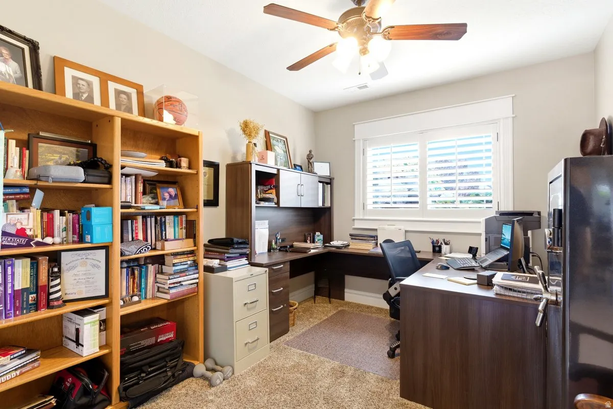 Dedicated room featuring a built-in wooden bookshelf, corner desk unit with integrated storage, and a ceiling fan with light fixture