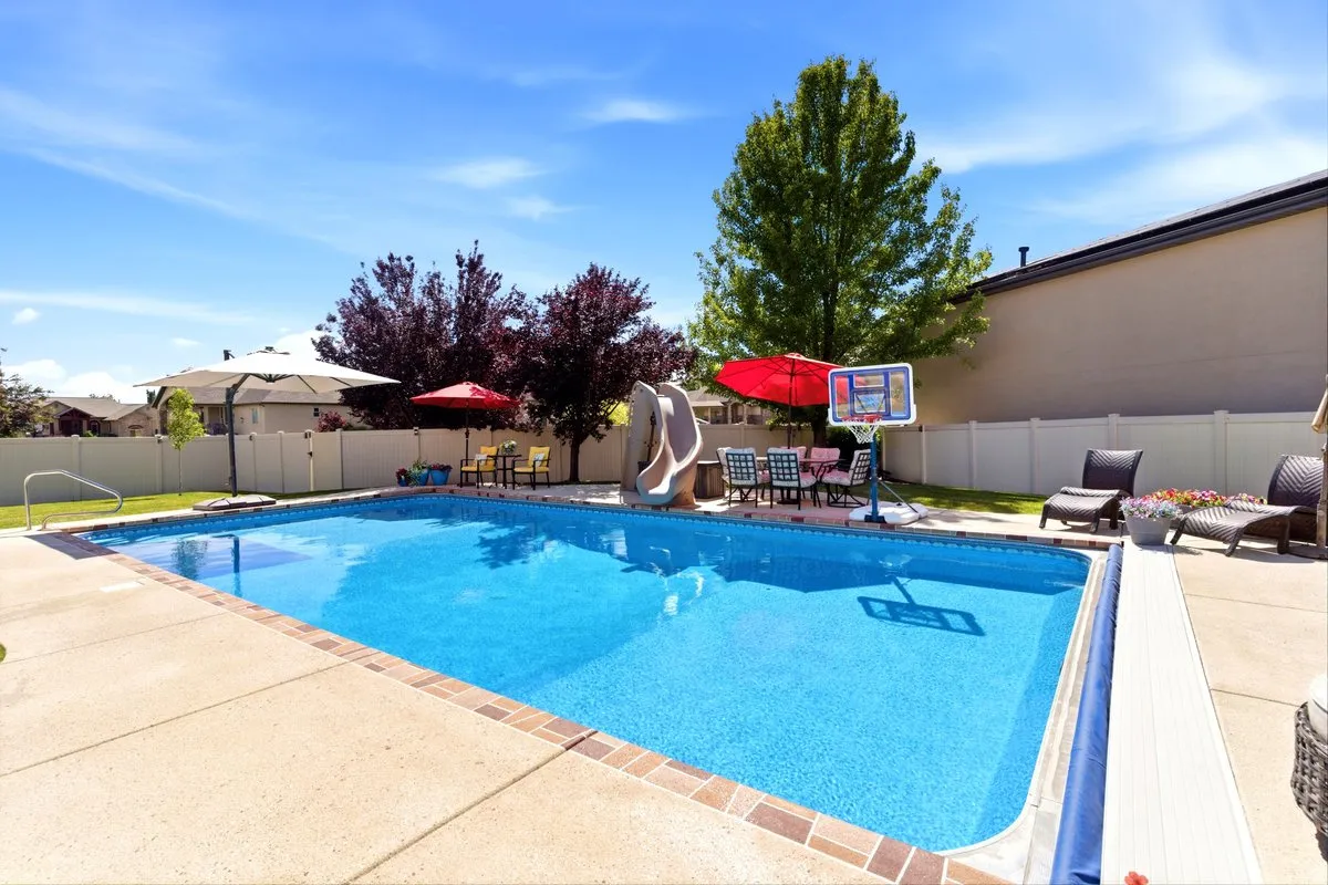 In-ground swimming pool featuring a perimeter of concrete decking with brick accents