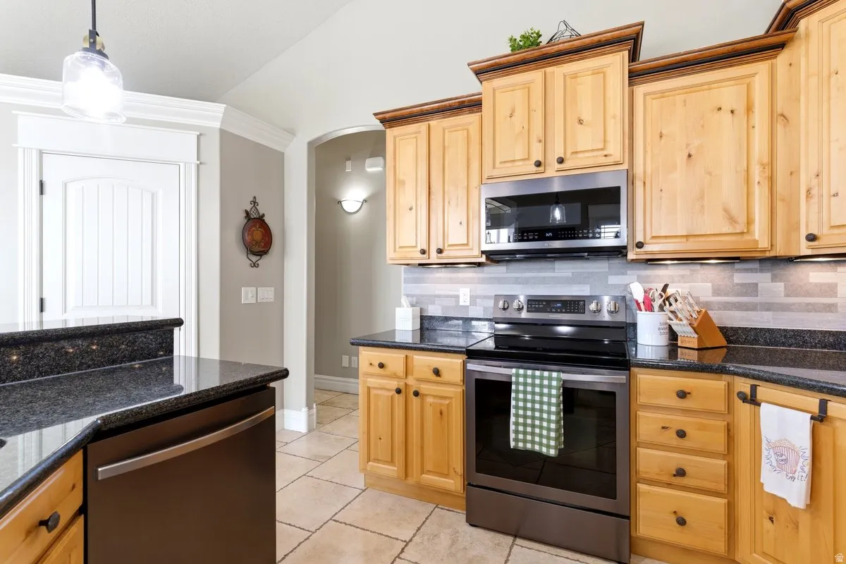 Kitchen featuring light wood cabinetry with dark hardware, black stone countertops, and a tile backsplash