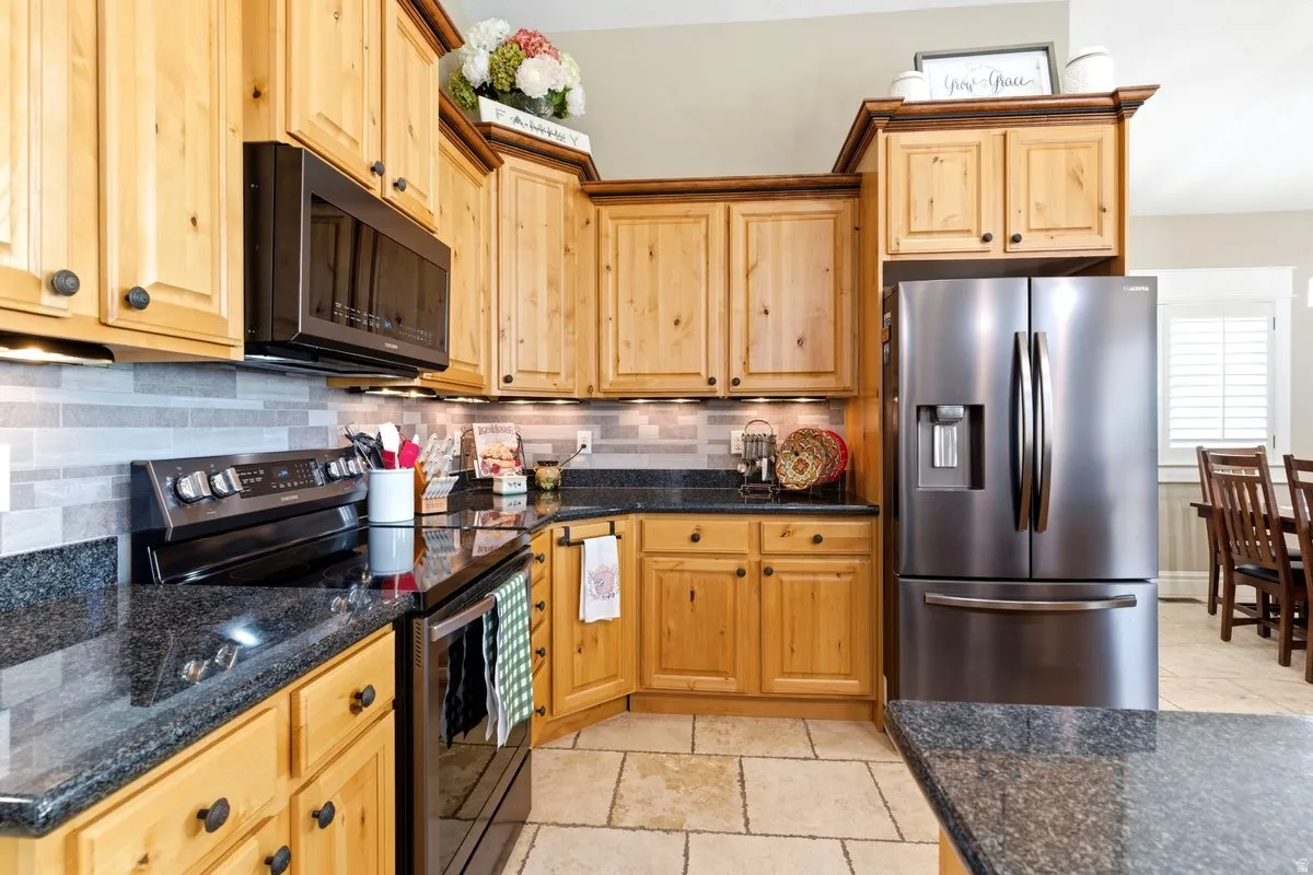 Kitchen featuring light wood cabinetry with dark hardware, dark countertops, and a tiled backsplash