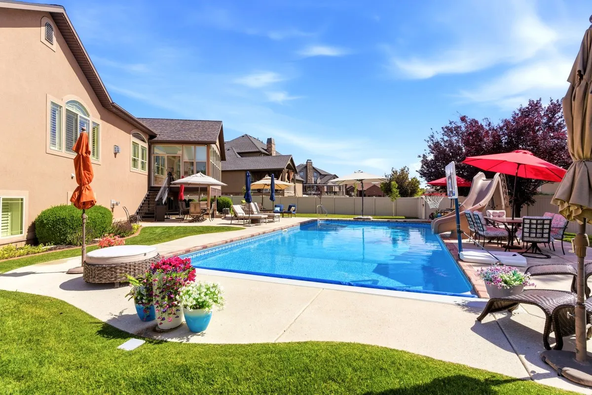 Expansive backyard featuring a rectangular swimming pool, concrete pool deck, and mature landscaping