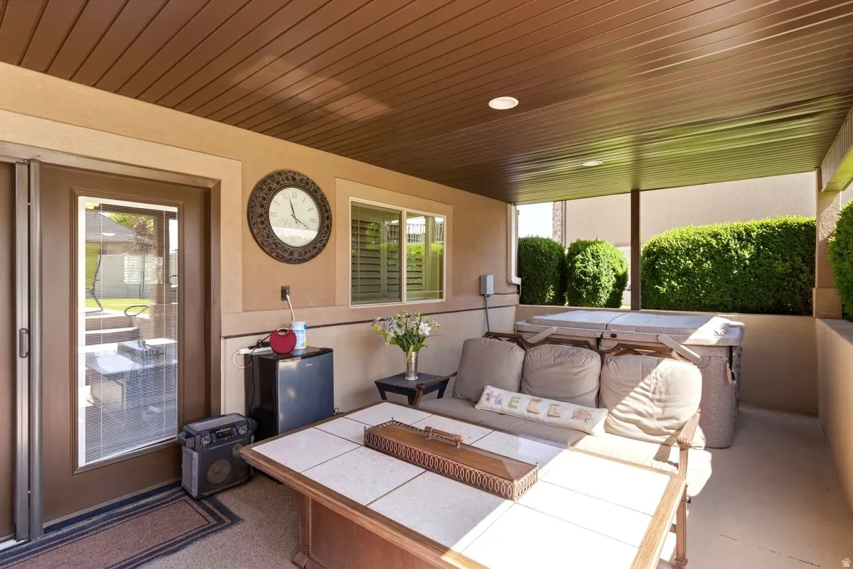 Covered outdoor patio featuring a neutral stucco exterior, a built-in spa, a sliding glass door, a window with horizontal blinds, and a brown paneled ceiling