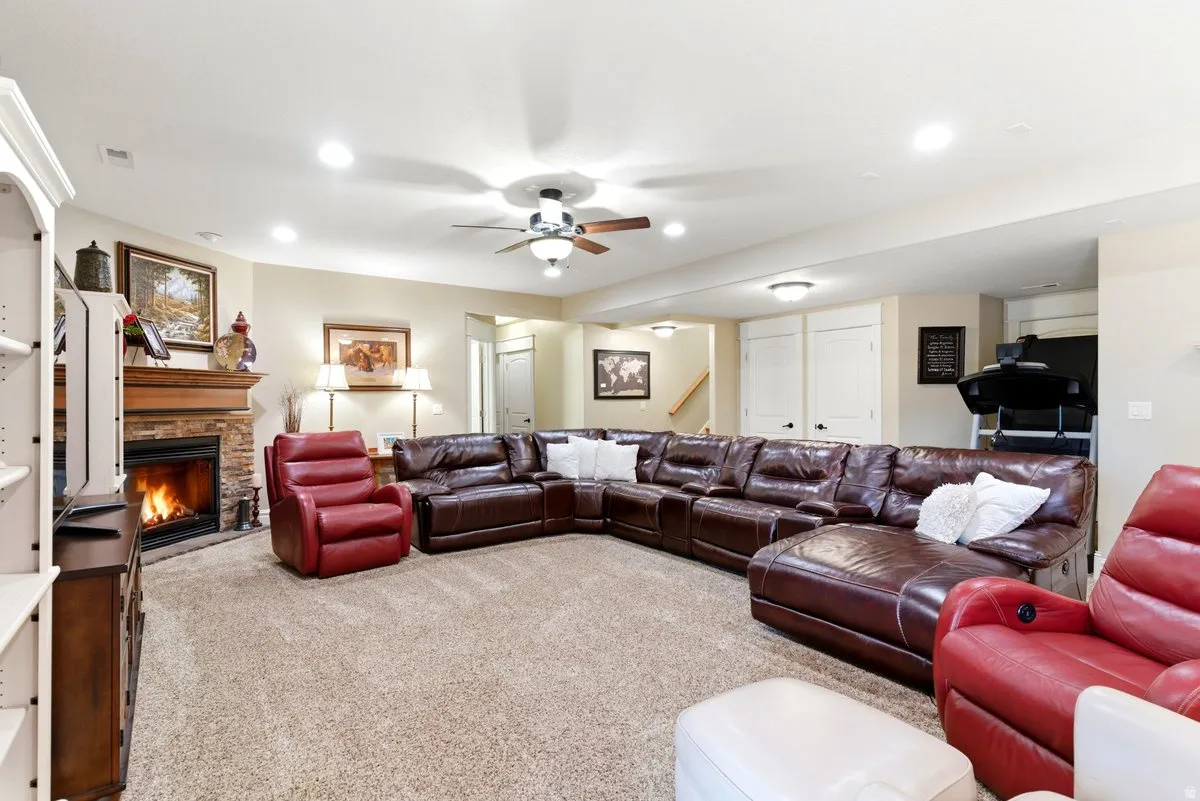 Spacious carpeted living area featuring a stone-faced fireplace with a wood mantle, recessed lighting, and a ceiling fan