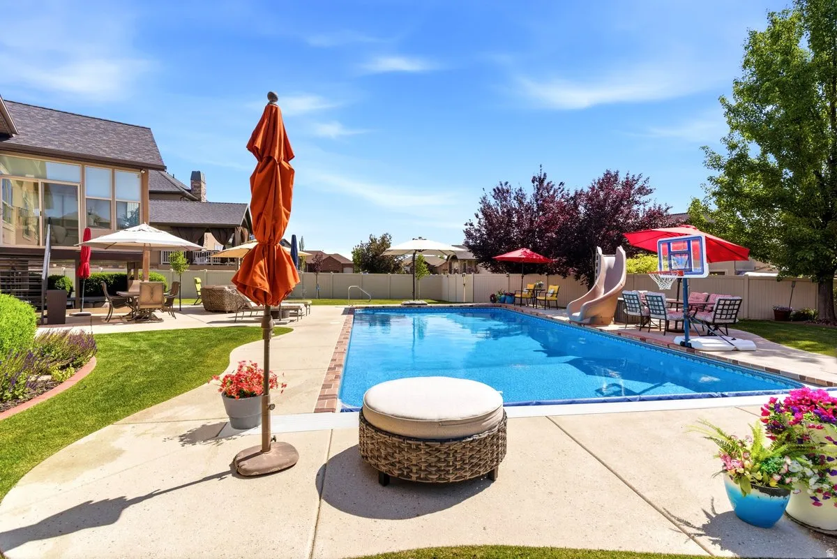 Expansive backyard featuring a rectangular swimming pool with brick coping, a surrounding concrete patio, and mature landscaping