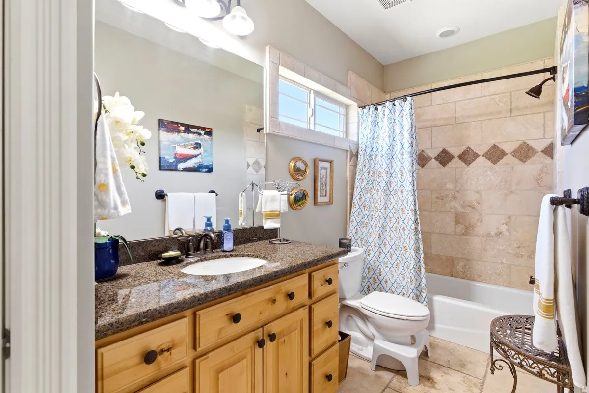 Bathroom featuring a light wood-finish vanity with a stone countertop and an undermount sink