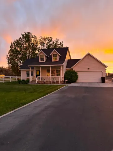Two-story residence featuring a covered front porch with white railings, dormer windows, an attached two-car garage, and a paved driveway