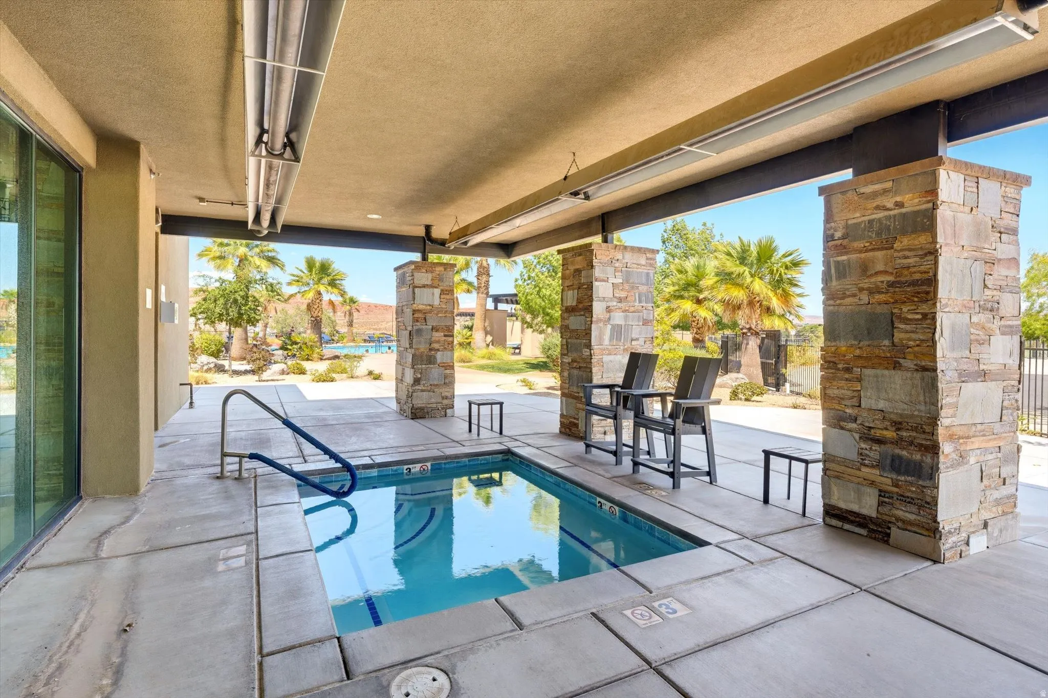 Covered patio featuring an in-ground spa with a handrail, stone-clad support columns, and an integrated ceiling heater