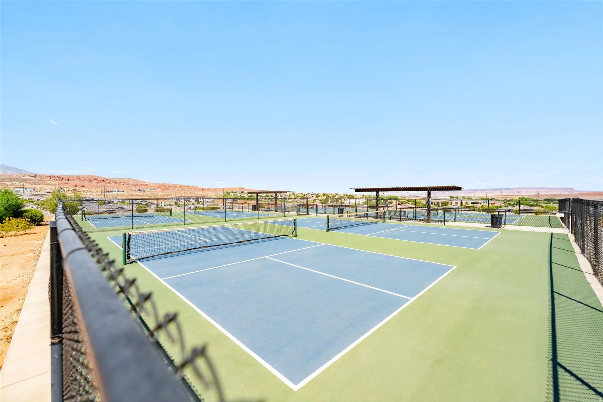 Community courts featuring multiple blue and green playing surfaces, chain-link fencing, and shaded structures