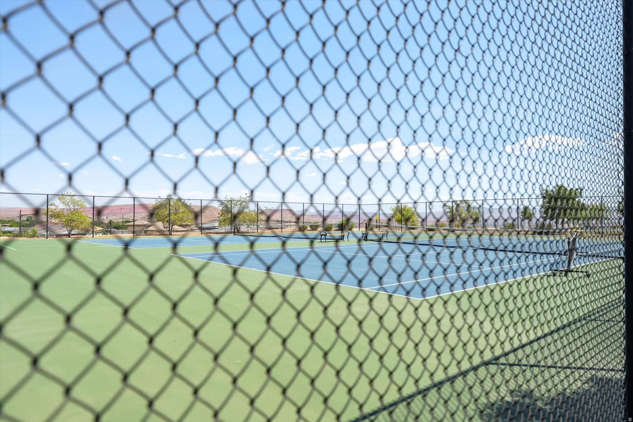 Outdoor tennis court featuring a two-tone playing surface, perimeter fencing, and distant mountain scenery